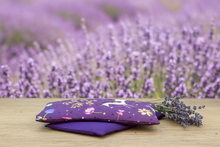 Load image into Gallery viewer, Two purple fabric swatches with unicorn and floral designs on a wooden surface.