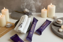 Load image into Gallery viewer, Packaged Lavender Refreshment Towel with a stack of 3 rolled towels outside of the packaging