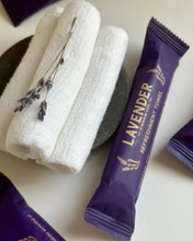 Load image into Gallery viewer, Packaged Lavender Refreshment Towel with a stack of 3 rolled towels outside of the packaging

